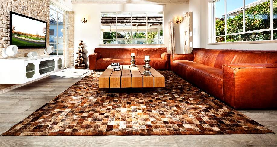 שטיח מריבועי עור במראה של שמיכת טלאים, בסלון בעל ספות חומות-אדמדמות. "שטיחי איתמר"